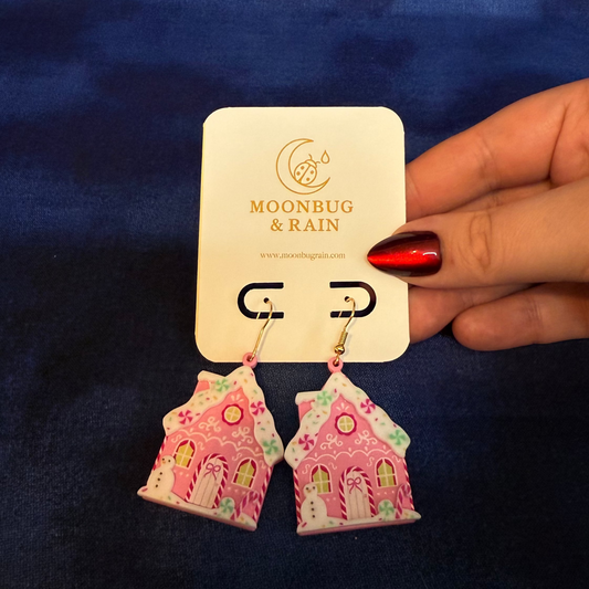 Pink house-shaped earrings on a 'Moonrug & Rain' card against a blue background