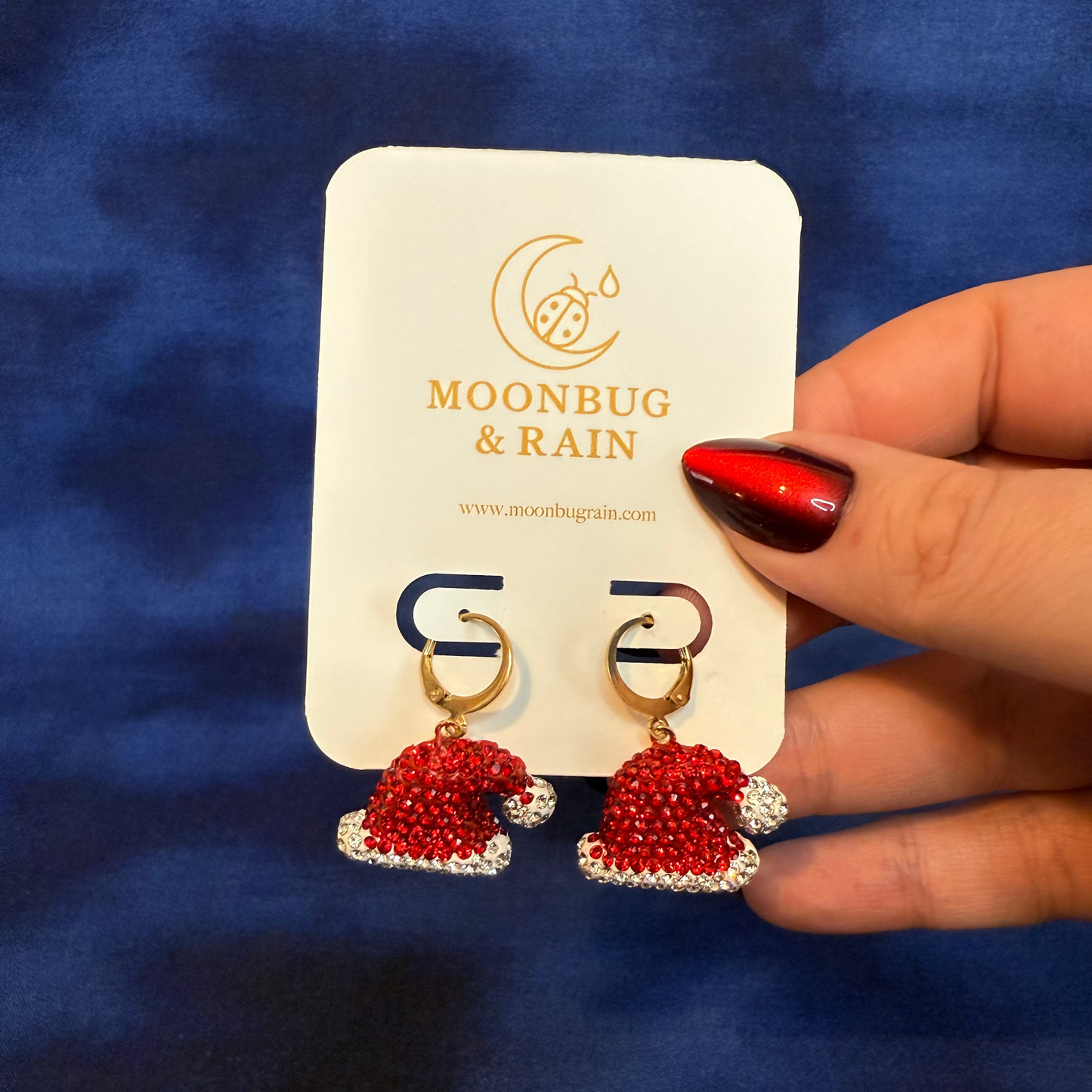 Red beaded earrings on a 'Moonbug & Rain' card against a blue background