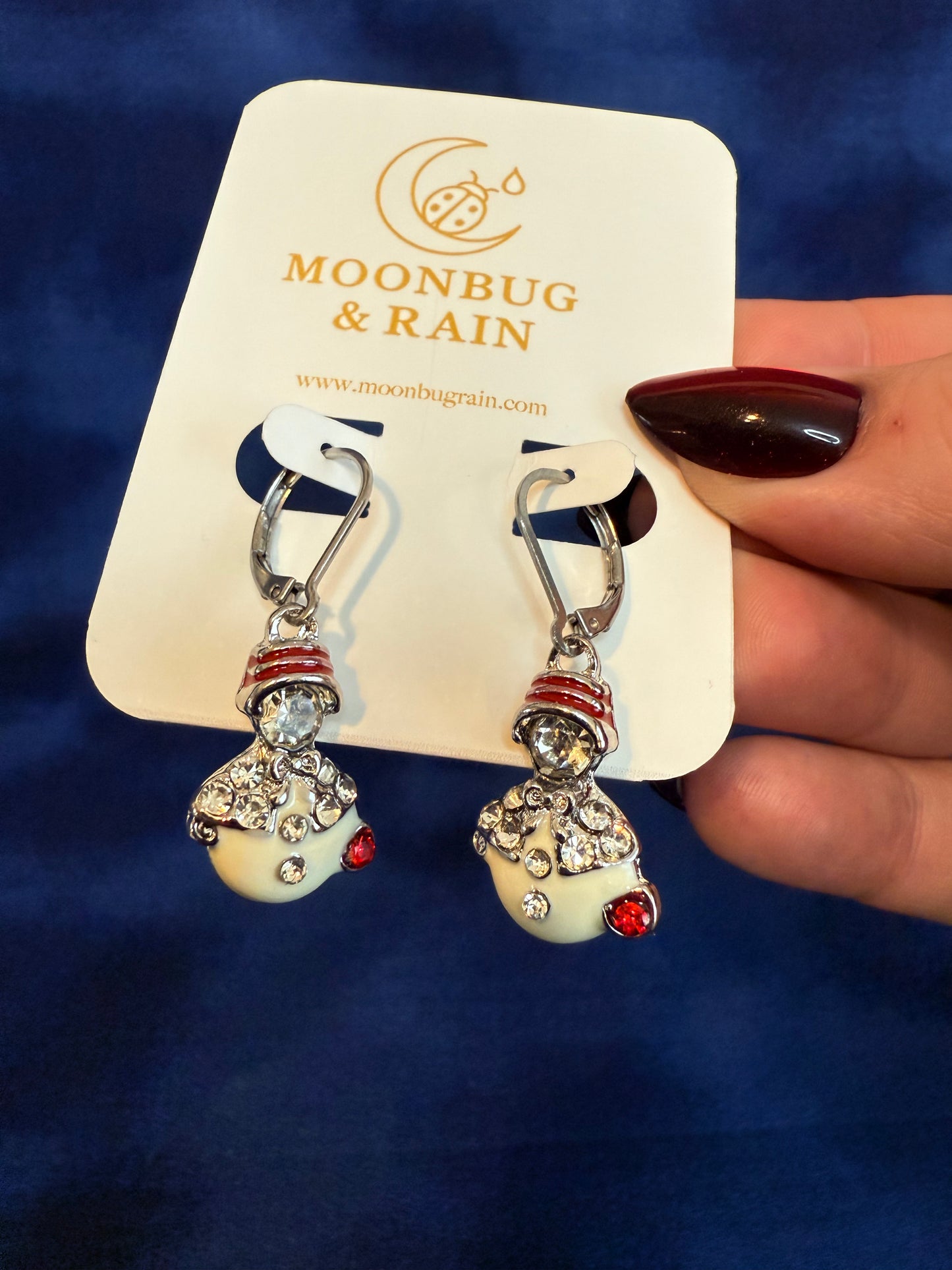 Pair of earrings on a Moonbug & Rain branded card against a blue background