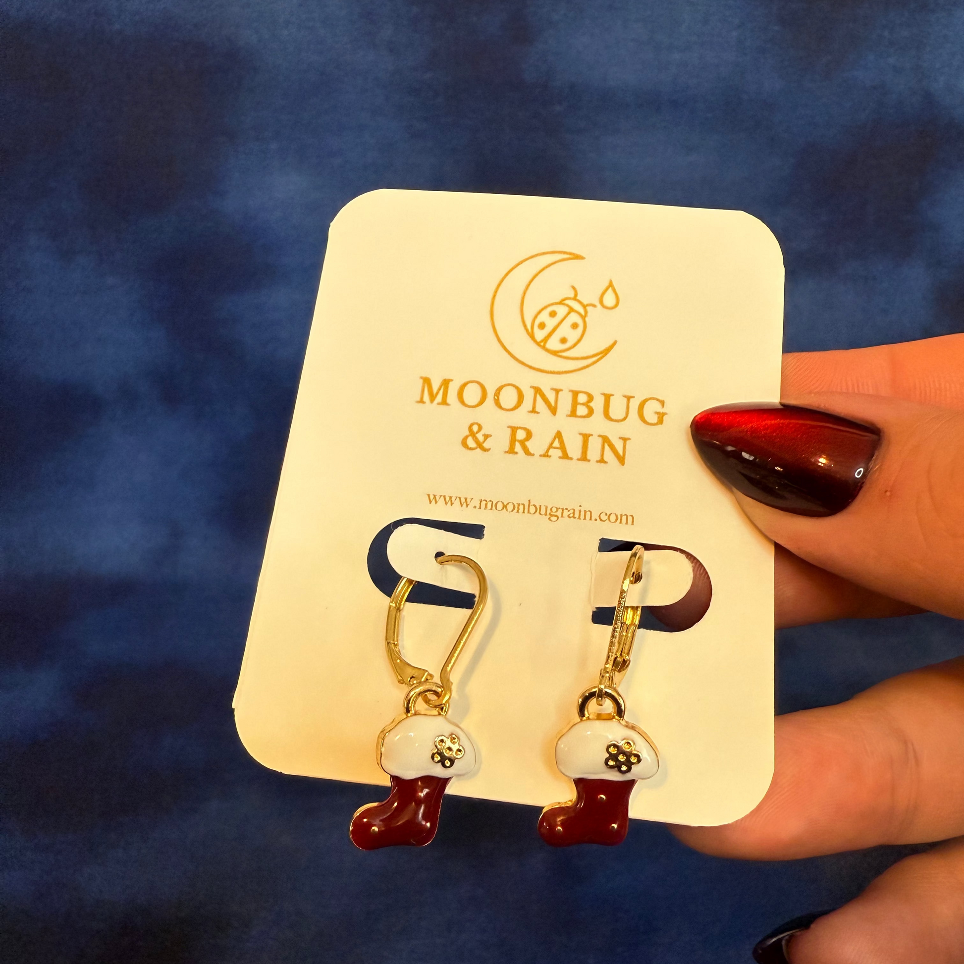 Earrings on a 'Moonbug & Rain' card held against a blue background