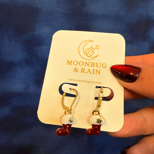 Earrings on a 'Moonbug & Rain' card held against a blue background