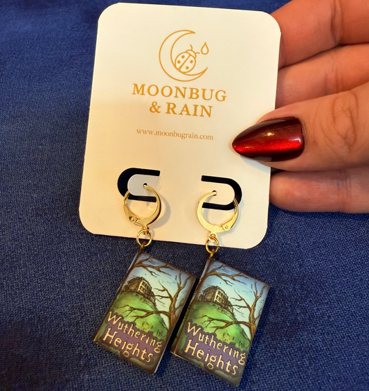 Earrings with 'Wuthering Heights' design on a Moonbug & Rain card against a blue background.
