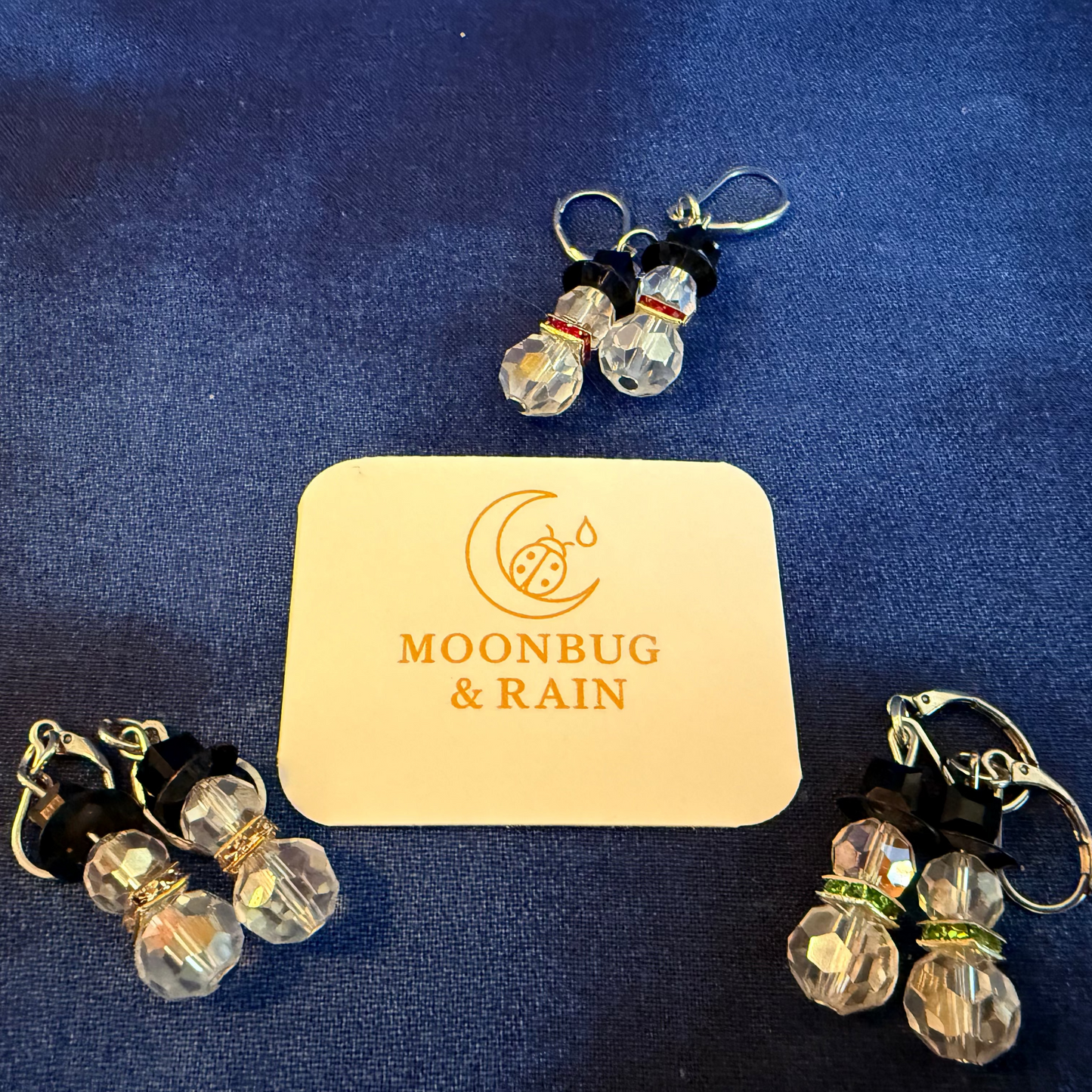 Pair of earrings with 'Moonbug & Rain' card on a blue background