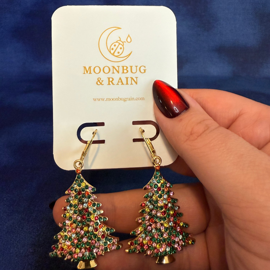 Tree-shaped earrings on a 'Moonbug & Rain' card against a blue background