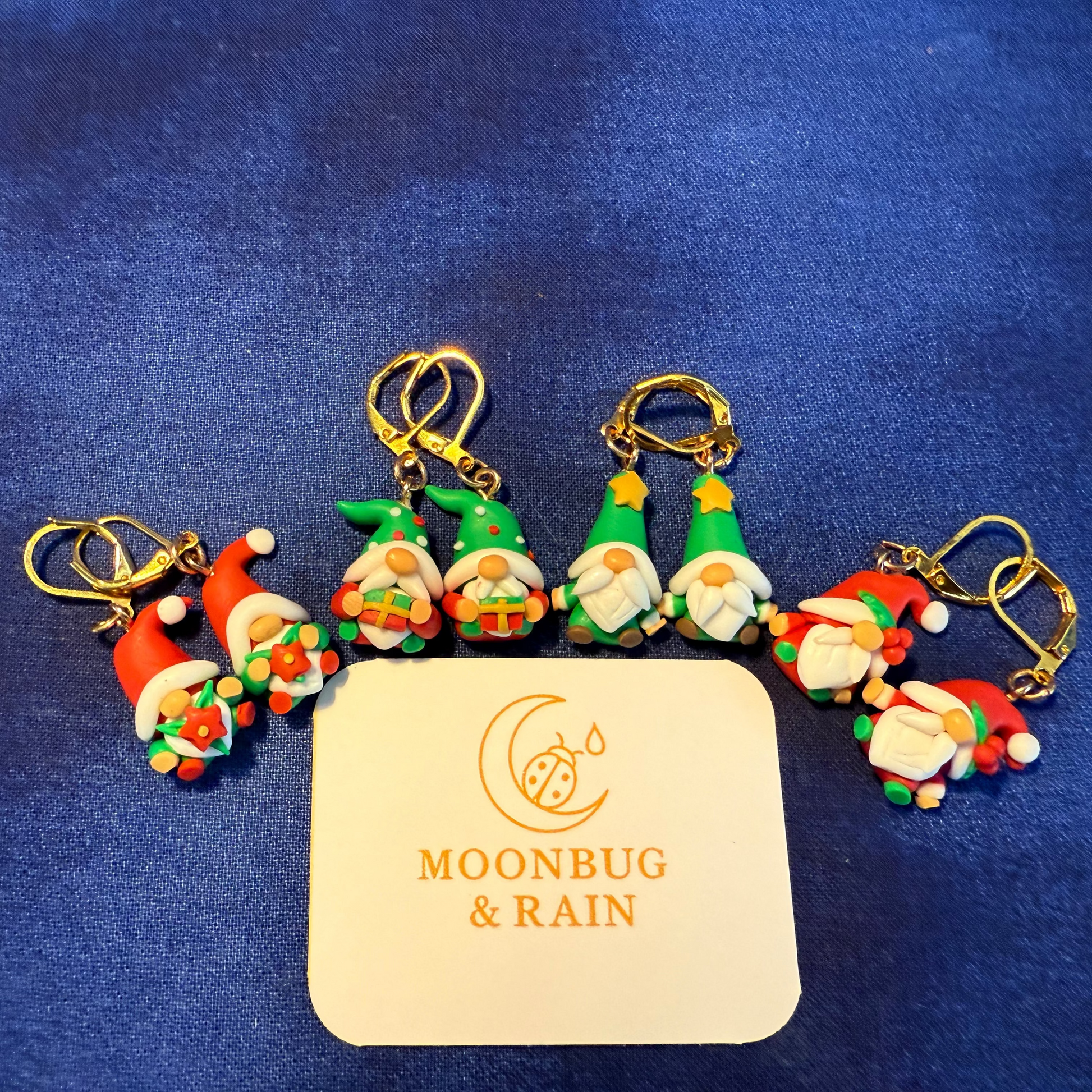 Set of gnome-shaped keychains with a 'Moonbug & Rain' branded card on a blue background