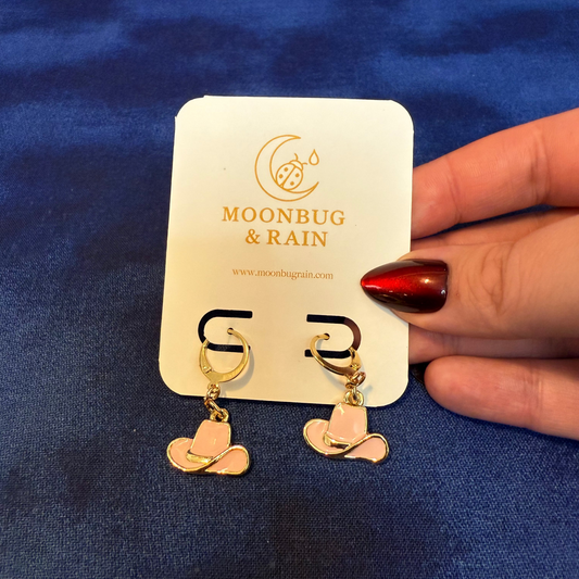 Gold and pink cowboy hat earrings on a 'Moonbug & Rain' branded card against a blue background.